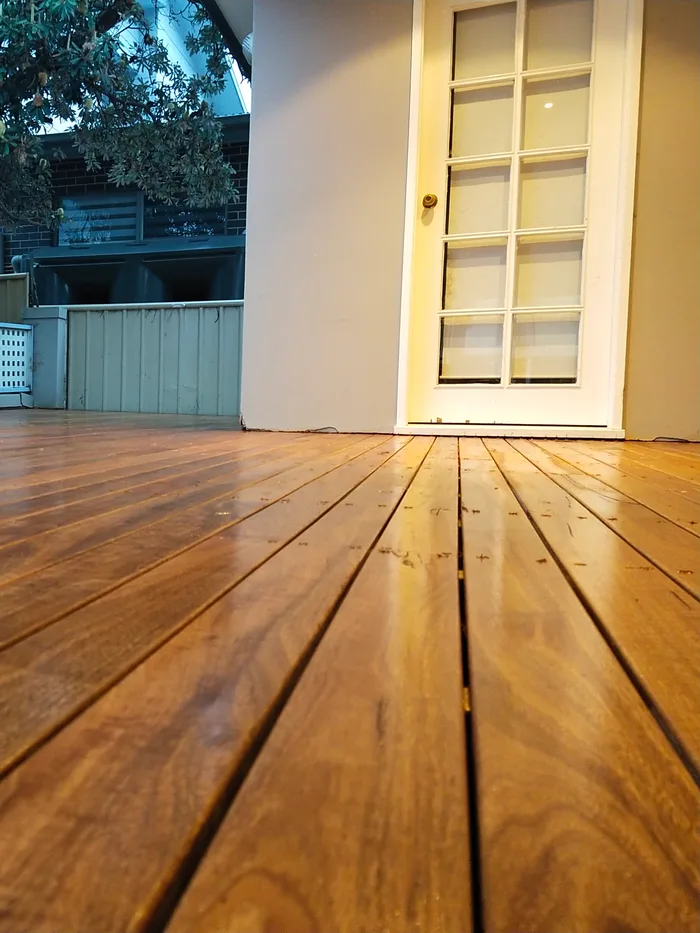 Freshly oiled timber decking boards running towards a white glass-panelled door, shot low along the deck