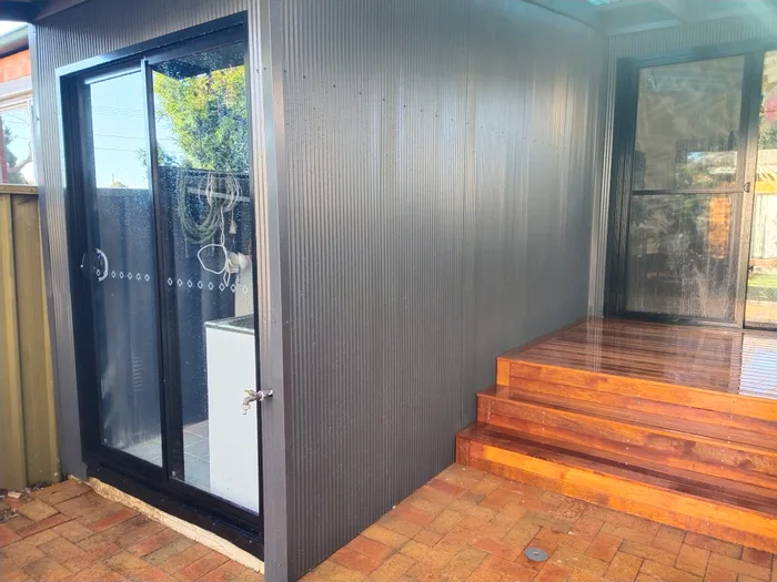 New timber steps leading up to a deck beside a dark corrugated shed with a sliding door