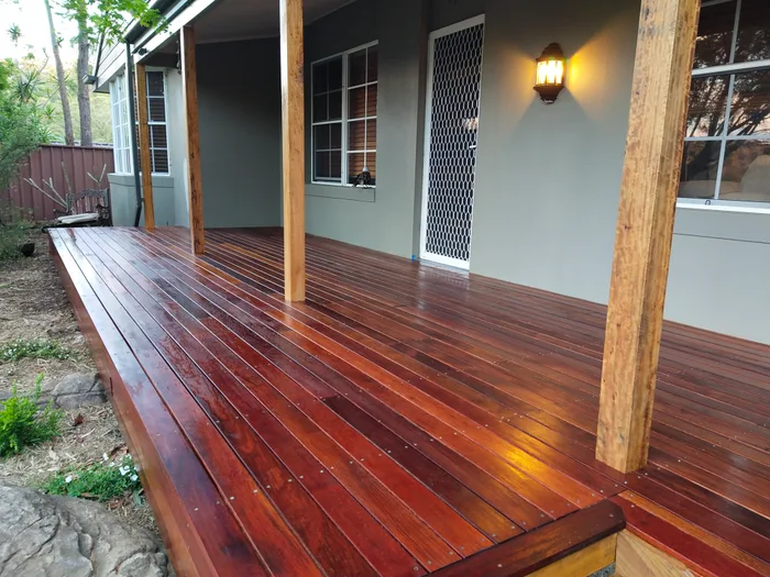 Covered timber verandah deck with hardwood posts, freshly oiled boards and a lit wall lantern beside the front door