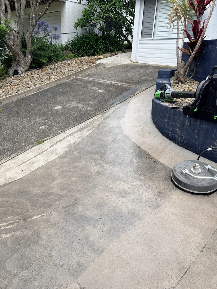 Pressure washing a concrete driveway in progress: the cleaned half is pale and the uncleaned half is still grey, with the surface cleaner sitting on the concrete